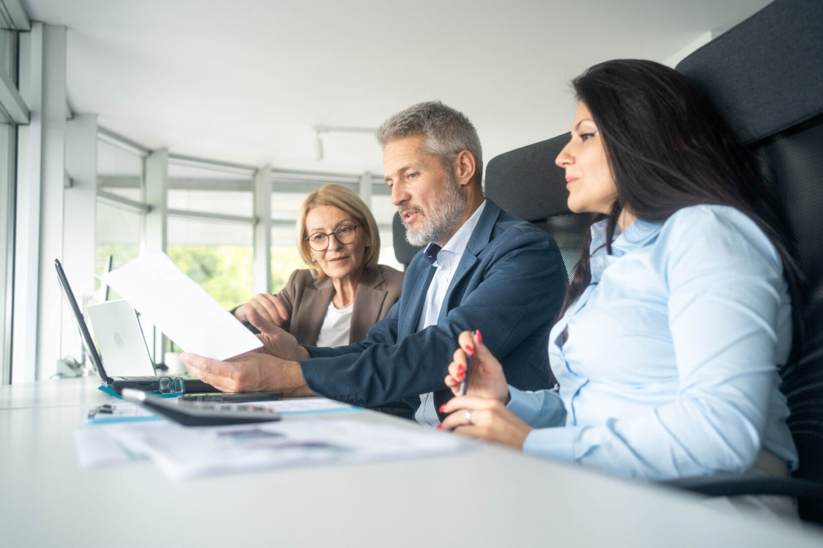 Three professionals reviewing documents in a bright office.