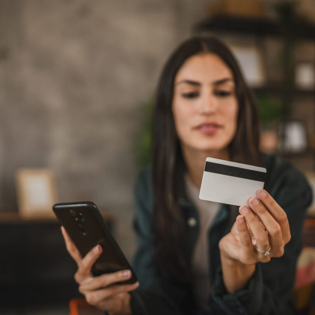 A woman holding a credit card and phone, ready to make an online purchase.