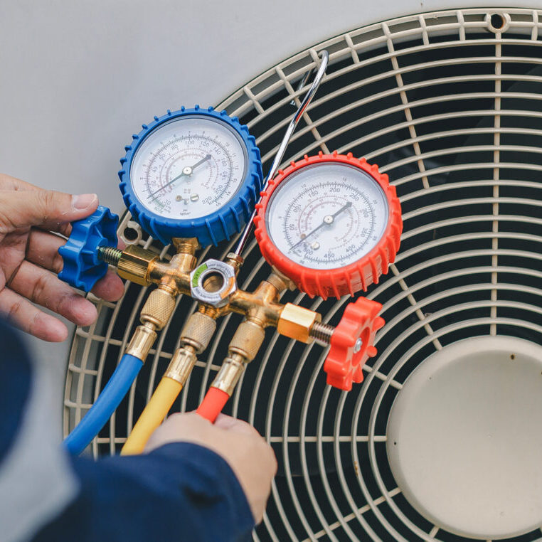 Technician checking HVAC pressure gauges on air conditioning unit.