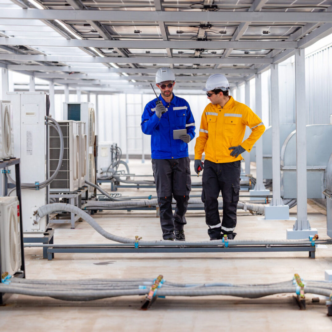 Two workers in safety gear inspecting pipes in an industrial setting.
